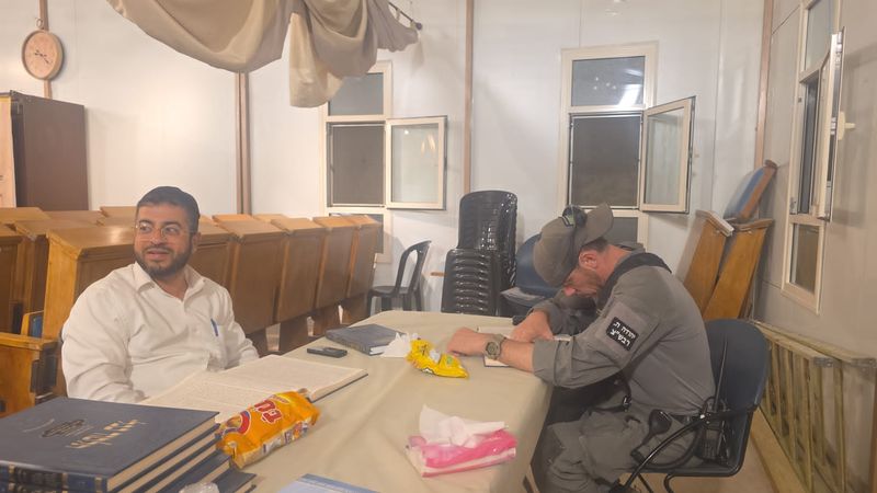 אברך ושוטר מג״ב לומדים יחד ליד שולחן בבית הכנסת בשעת לילה
