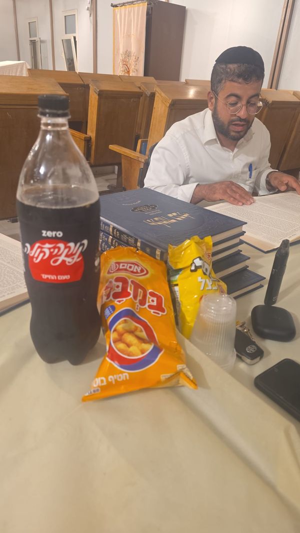 לומד יושב מול ערימת ספרים פתוחים, ועל השולחן כיבוד קל